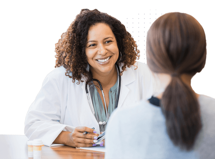 Smiling female doctor with a stethoscope around her neck talking to a female patient across the desk in a medical consultation